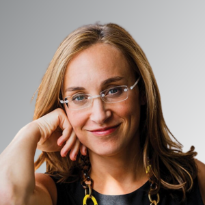 Image of Sara Gottlieb souris sur un fond gris, portant des lunettes et un habit professionnel